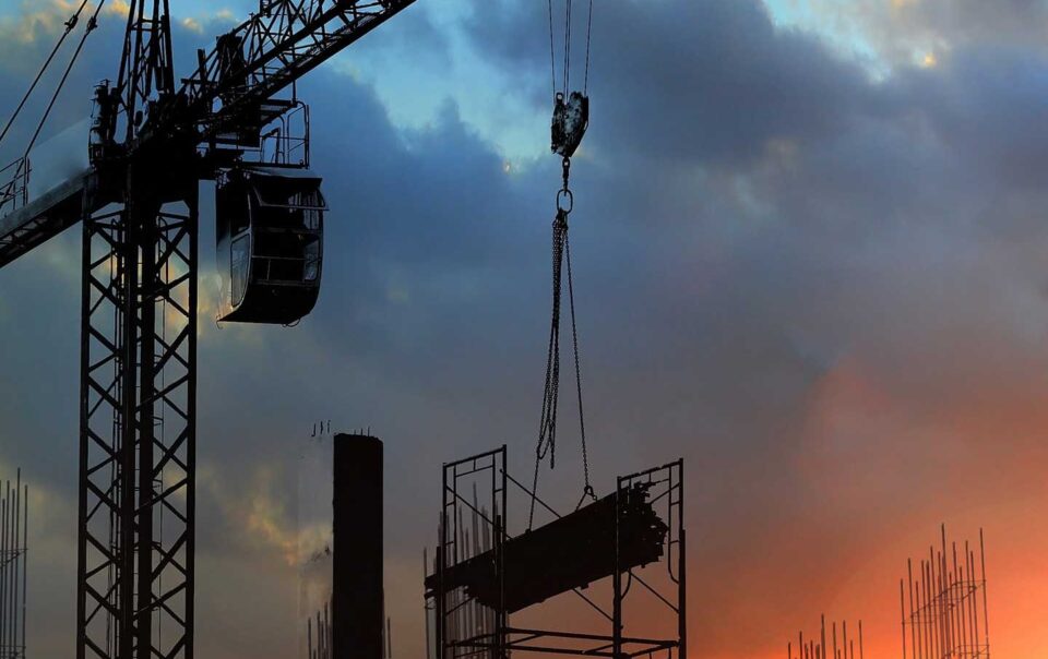 Construction crane carrying work materials at dusk.