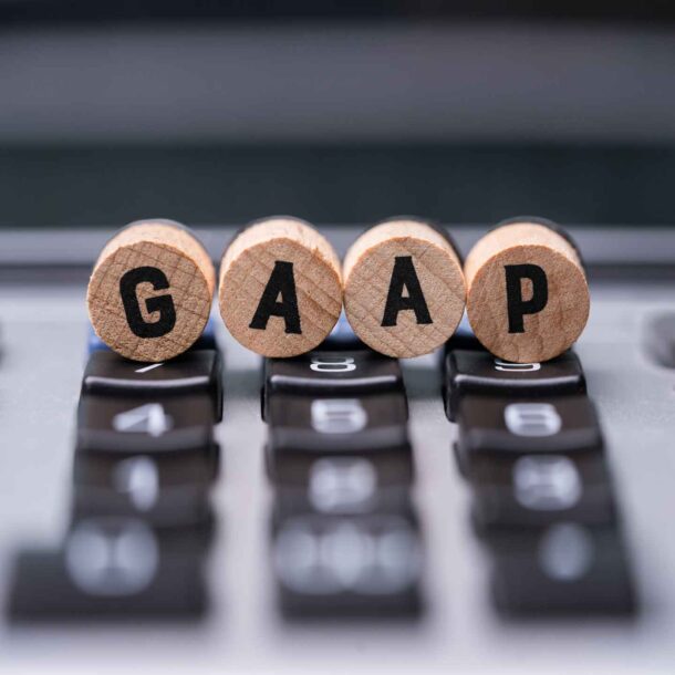 Round wooden dowels with the letters GAAP on the front of them resting on a calculator.