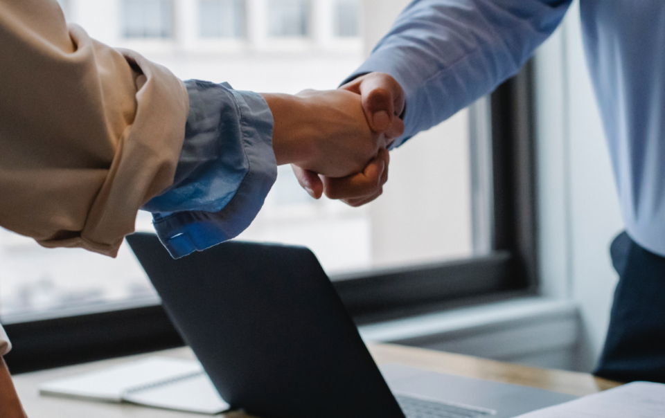 Two Caucasian people shaking hands over a desk.