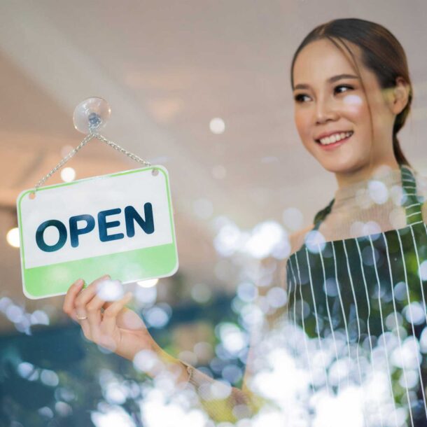 Asian woman business owner holding open sign