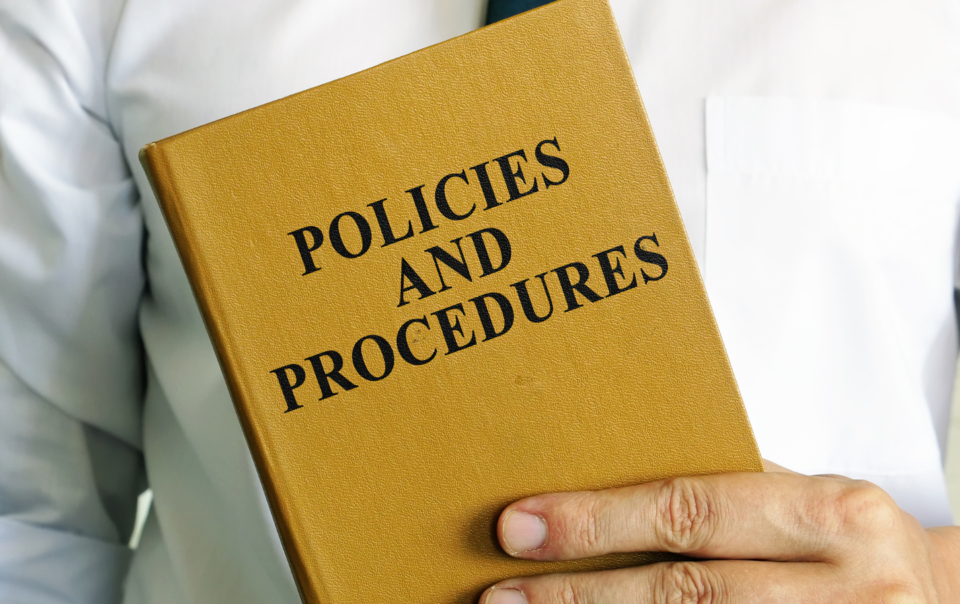A man holding a yellow book titled Policies and Procedures