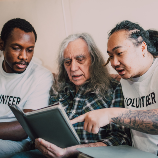 Two Volunteers Reading a Book to an Elderly Gentleman