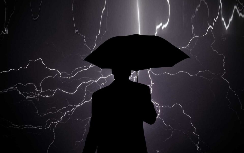 silhouette of businessman holding umbrella facing lightning storm