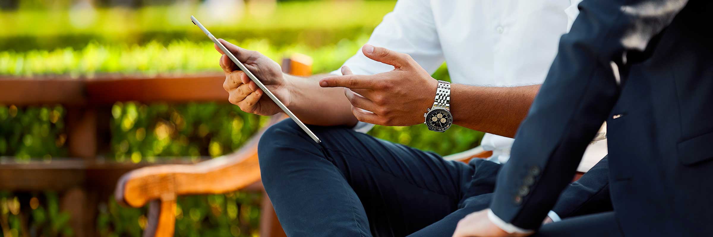 Two businessmen on a park bench reviewing financial information on a tablet