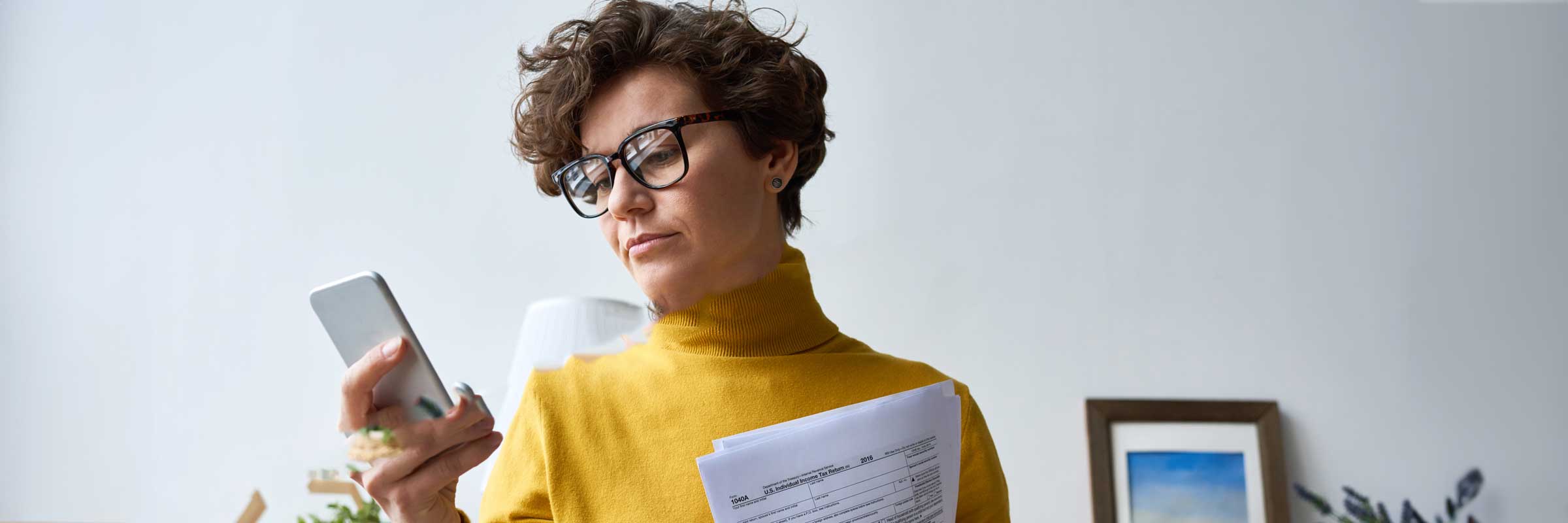 Woman looking at her phone while holding tax forms.
