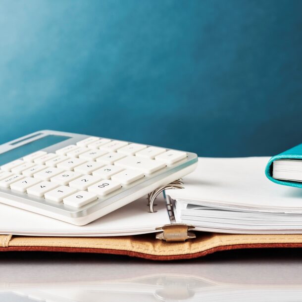 Up close image of a calculator and mini notebook resting on a 3-ring binder.