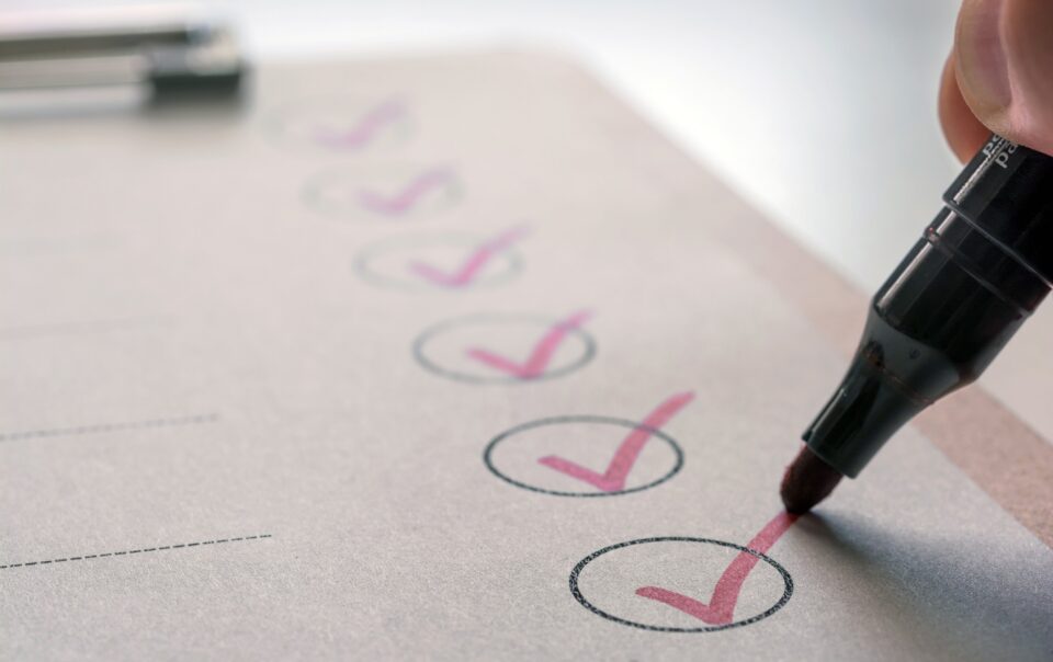 Close-up of a red highlighter marking check circles on a printed checklist, indicating completing tasks.
