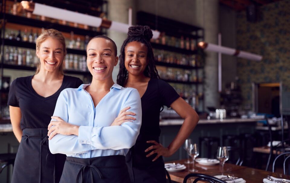 Image of three restaurant employees standing in front of the bar and smiling at the camera.