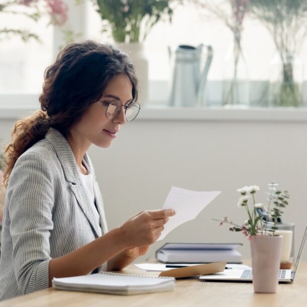 Photo of woman sitting at a desk looking at a document in hand.