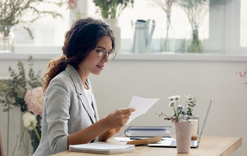 Photo of woman sitting at a desk looking at a document in hand.