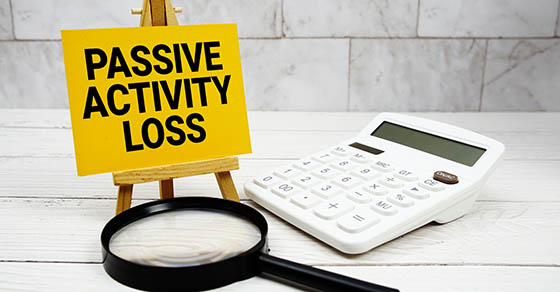 Image of a small easel with a yellow poster reading "Passive Activity Loss" and a magnifying glass underneath with a calculator off to the right.