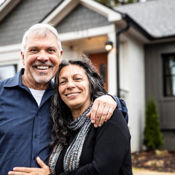 Two adults standing together in front of a residential home, illustrating family estate planning and asset transfer.