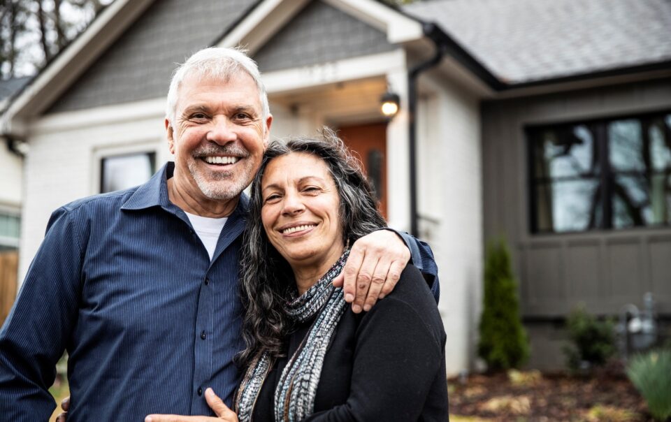 Two adults standing together in front of a residential home, illustrating family estate planning and asset transfer.